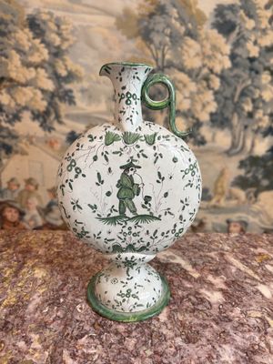 un vase blanc muni d'une anse verte, posé sur une table