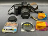 a camera, a lens, a camera case, and other items laid out on a table