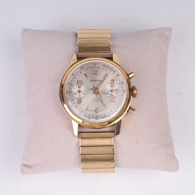 une photo d'une montre en or posée sur un oreiller, sur une surface blanche