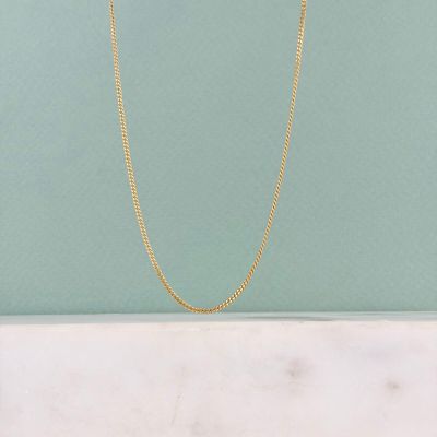 un collier à chaîne en or posé sur un plan de travail en marbre