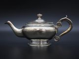 a silver teapot on a table with a black background