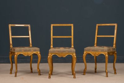 pair of gilded chairs with upholstered seats against a blue wall