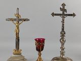 deux croix en argent et en or et un verre rouge posés sur une table