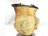 un petit vase orné d'un visage, dans une boîte transparente