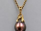 a black pearl and gold pendant on a gold chain