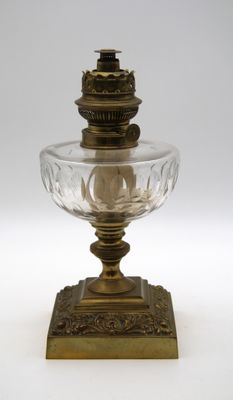 une lampe à huile ancienne en verre et laiton, posée sur un pied, sur fond blanc