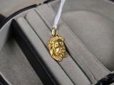 un pendentif en or orné d'un visage, présenté dans un écrin