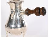 une cafetière en argent avec une poignée en bois, posée sur un socle