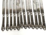 eight silverplated knives are lined up on a white surface
