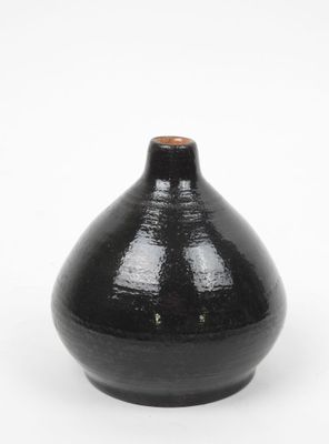 un vase noir surmonté d'un couvercle marron, posé sur une surface blanche