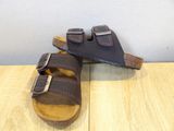 pair of brown sandals on a wooden table with a white wall in the background