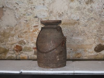 un grand vase marron posé sur une table devant un mur de pierre