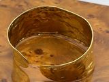 gold plated cuff bracelet on a wooden table with a white background