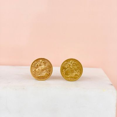 a pair of gold coin stud earrings sitting on top of a marble block