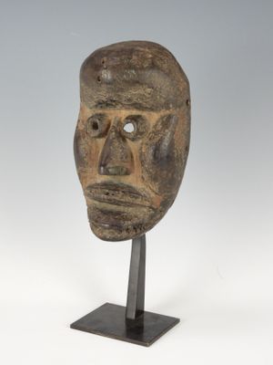 un masque en bois posé sur un socle, devant un fond blanc