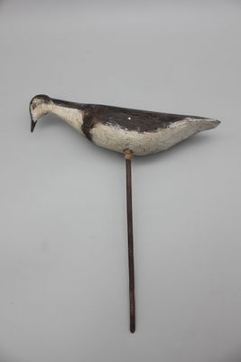 une image représentant un canard en bois fixé sur un bâton, posé sur une surface blanche