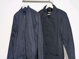two jackets hanging on a clothes rack against a white wall
