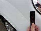 a person holding a ruler in front of a white car