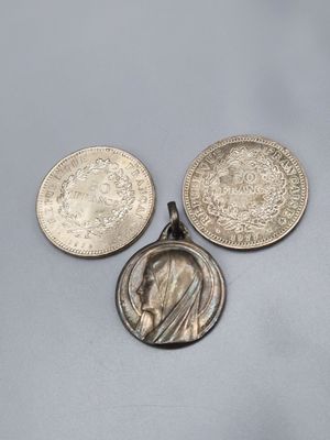 three silver coins and a silver pendant on a gray surface