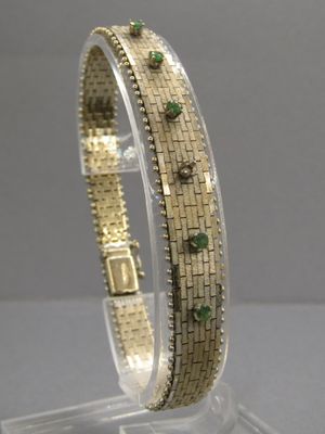 un gros plan sur un bracelet en or orné de pierres vertes