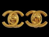 a pair of gold toned chanel earrings on a black background