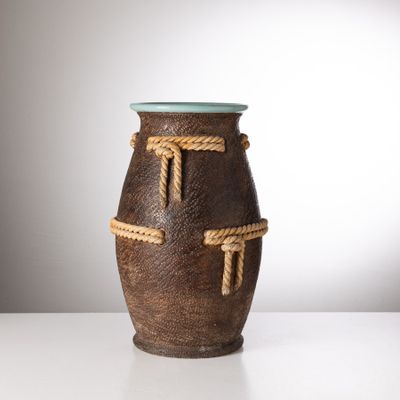 un vase marron entouré d'une corde, posé sur une table blanche