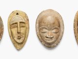 quatre masques en bois sont alignés sur une surface blanche