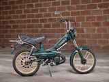 a small green motorcycle parked in front of a brick wall