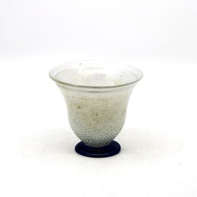 un petit bol en verre avec un socle noir posé sur une surface blanche
