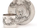a silver cup and saucer sitting next to a plate