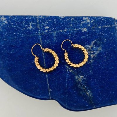 a close up of a pair of gold hoop earrings on a blue stone