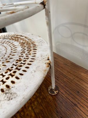 une chaise blanche dont l'assise est rouillée, posée près d'une table en bois