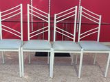 four white chairs with a glass table and a red wall