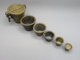 quatre tasses en laiton et un couvercle en laiton sont alignés sur une surface blanche