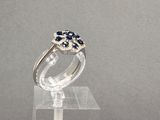 bague en argent sterling sertie de saphirs bleus et de diamants, posée sur un socle en acrylique transparent