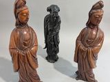 trois figurines en bois représentant des personnages asiatiques, posées sur un fond blanc