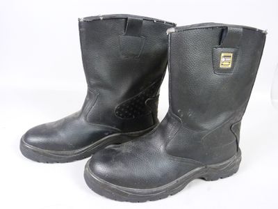 une paire de bottes de travail noires posées sur une surface blanche, sur fond blanc