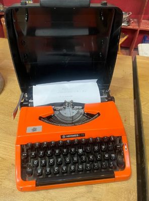 une machine à écrire orange posée sur une table, avec un clavier noir