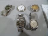 cinq montres exposées sur une table à côté d'un bloc-notes