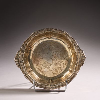 assiette en argent posée sur un support, sur une surface blanche avec un fond gris clair