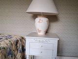 une table blanche sur laquelle est posée une lampe, à côté d'un lit