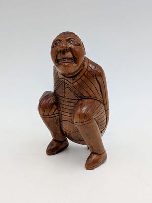 an old wooden figurine of a man squatting on a white surface