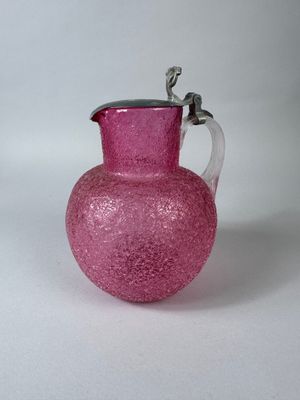 pink glass pitcher with a silver handle on a white surface