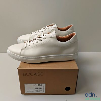 Les baskets blanches sont posées sur une boîte, elle-même posée sur une table.
