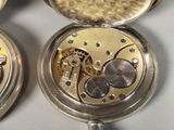 two silver pocket watches sitting next to each other on a table