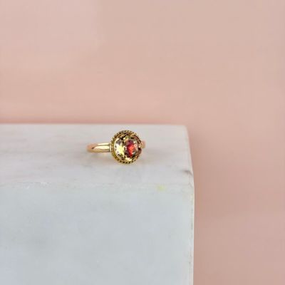 une bague en or sertie d'une pierre rouge, posée sur un bloc de marbre