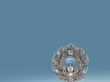 a close up of a brooch with a blue stone surrounded by diamonds