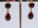 pair of gold and garnet stone drop earrings on a stand