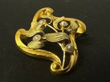 une image représentant une broche en or ornée de perles sur un fond noir