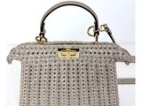 Le petit sac gris est en tissu tissé et possède une poignée en métal.